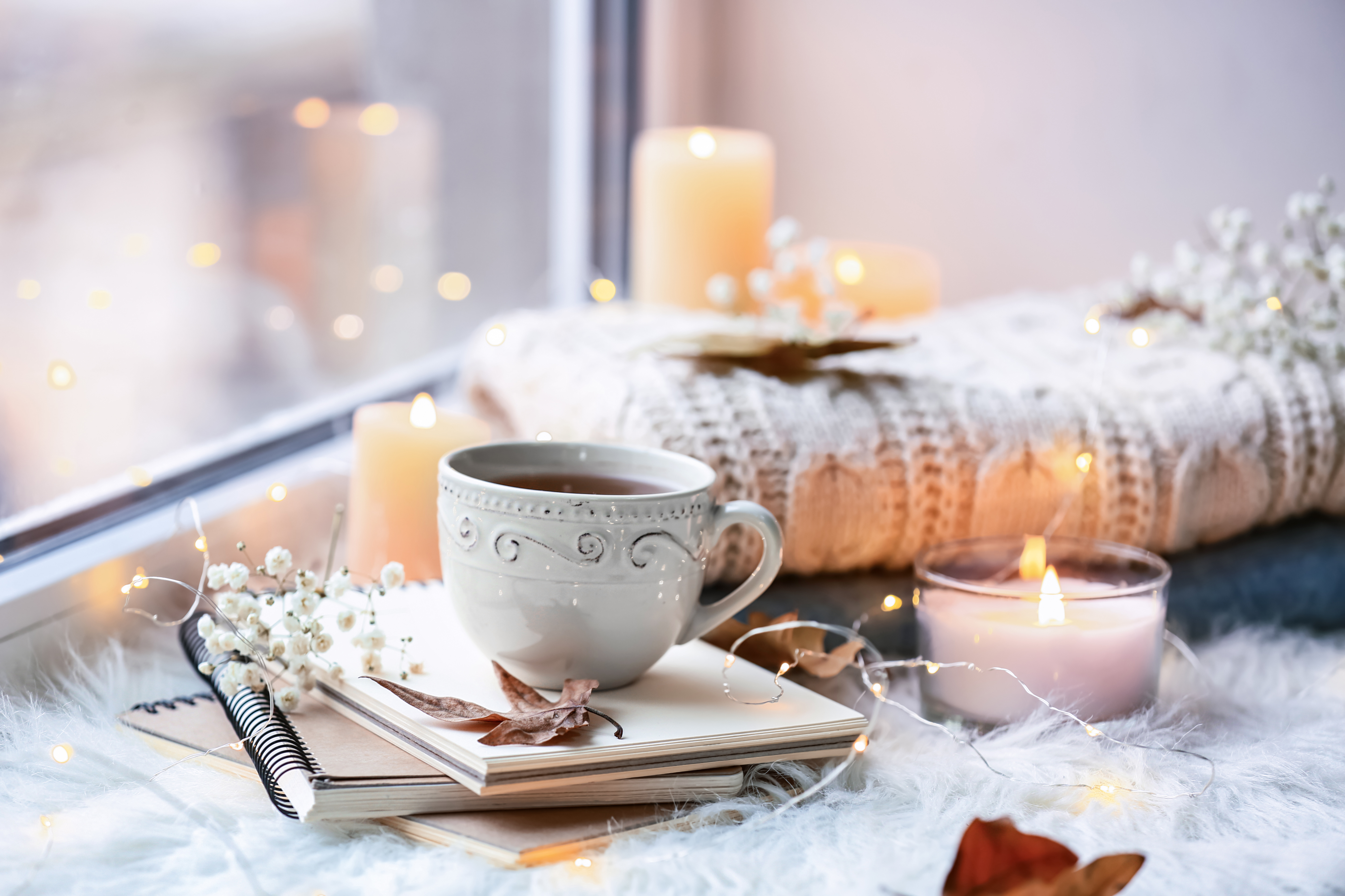 Two small lit candles and a warm cup on a wooden windowsill in soft evening light, a quiet corner at home