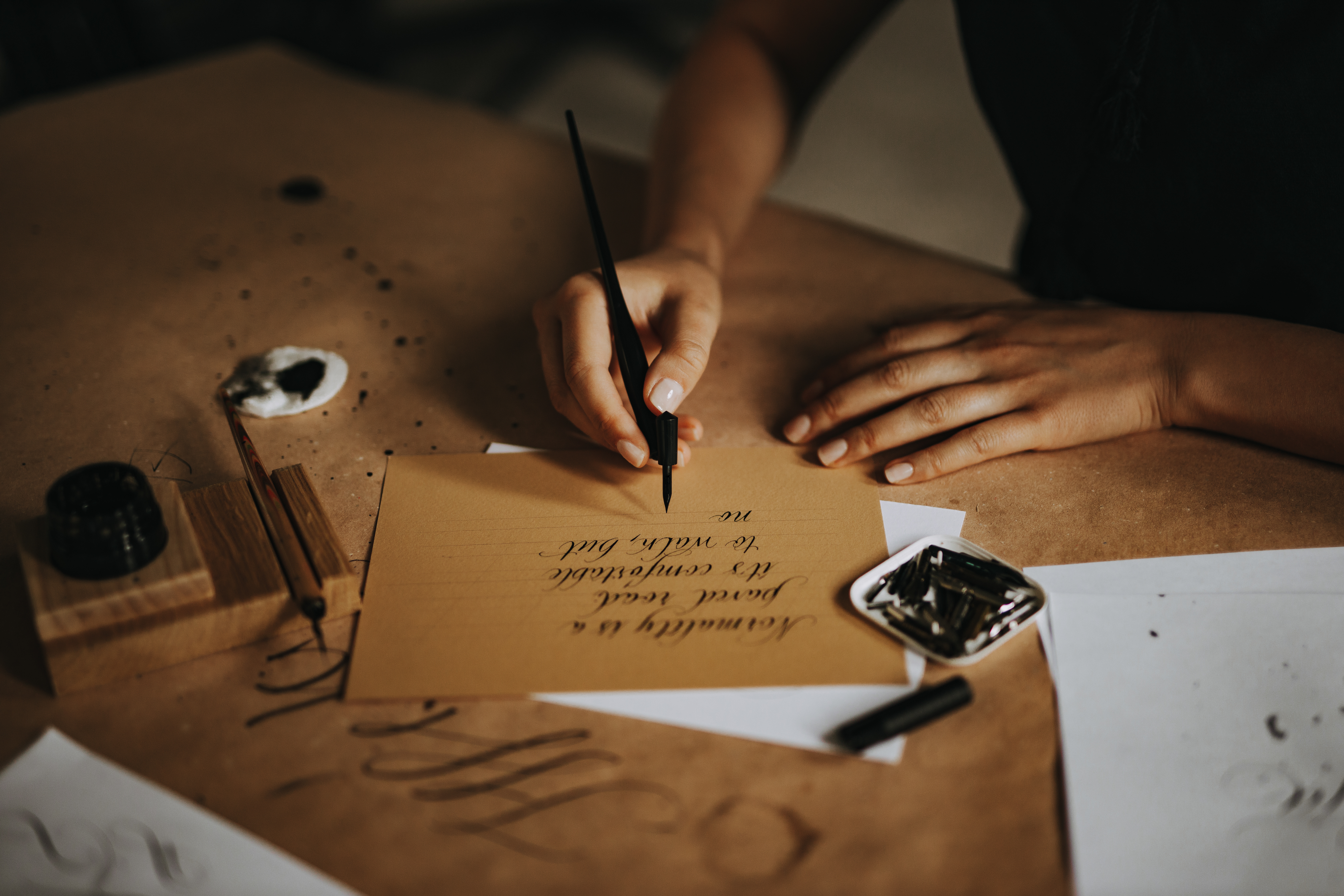 A hand writing a letter in ink on cream parchment, a quiet gesture of putting love into words after loss