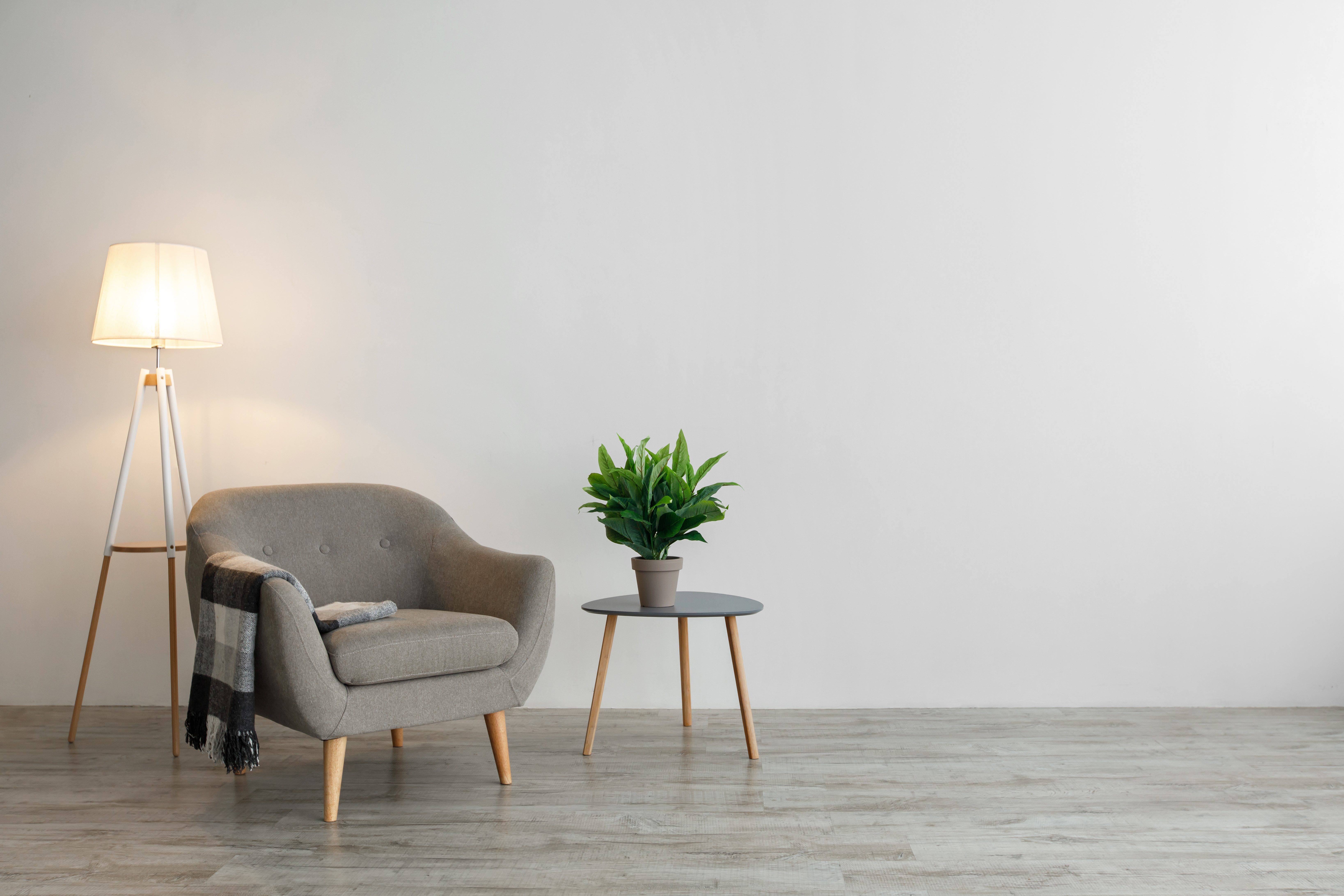 A quiet corner at evening, an armchair with a soft blanket beside a glowing lamp, a small plant on the table nearby