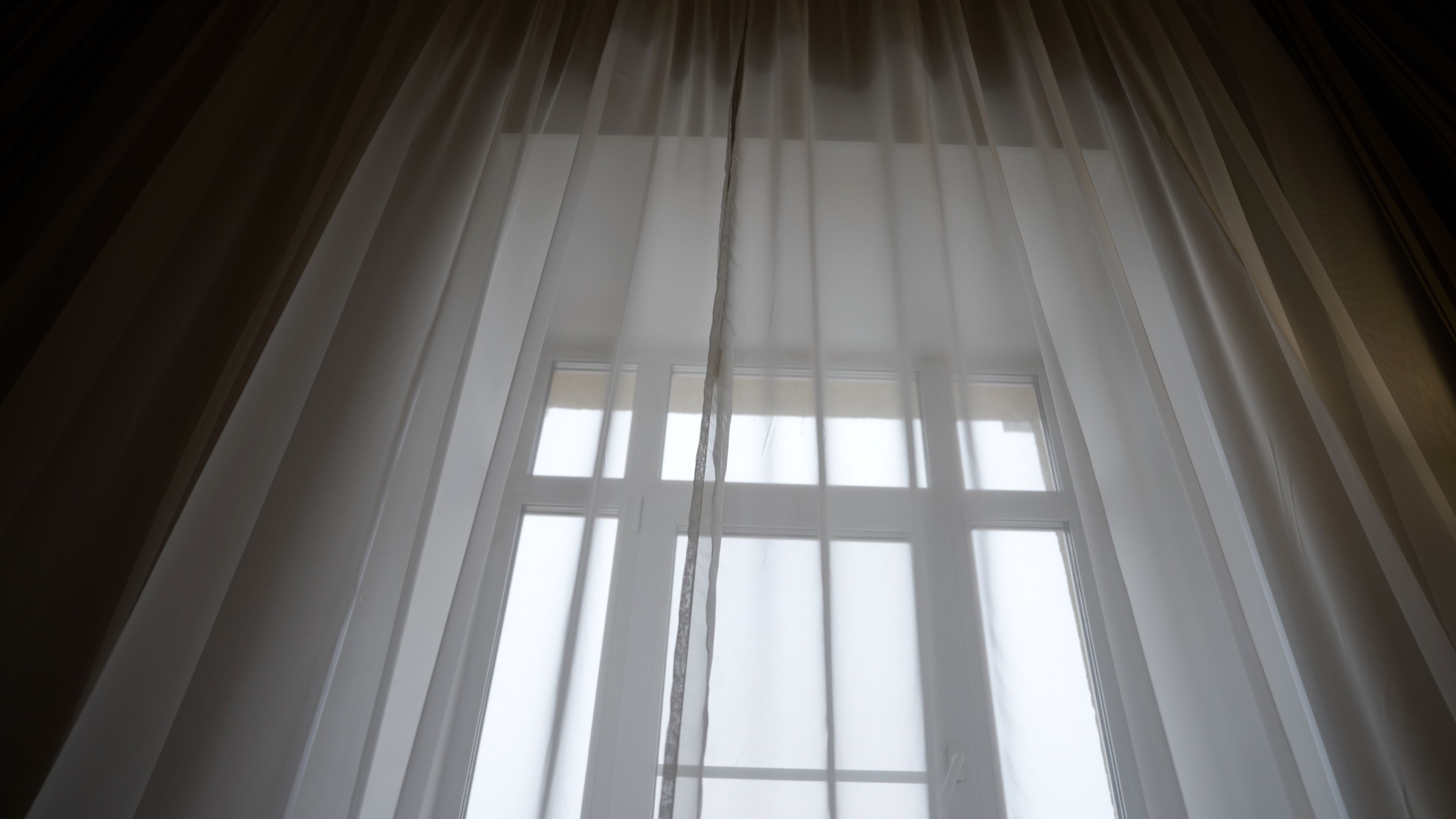 Sheer white curtains glowing with soft morning light in a quiet room, a calm and gentle space for grief