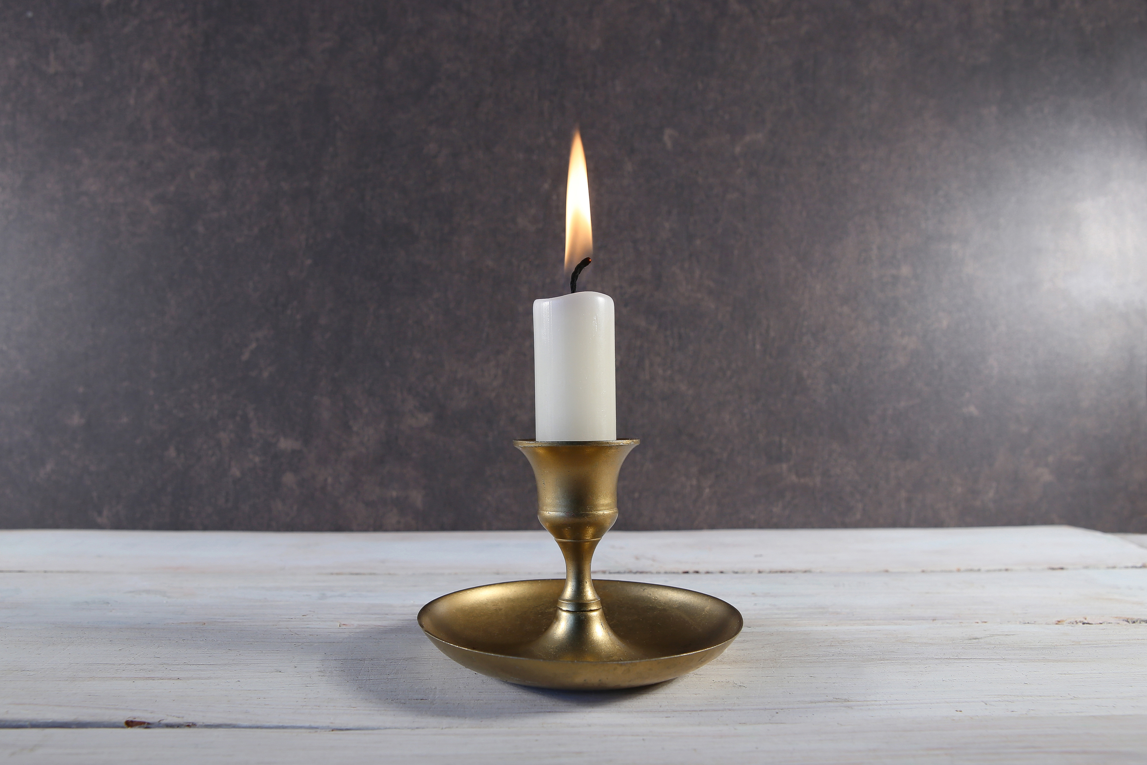 A single lit candle on a white wooden table, a small quiet way to acknowledge a baby before a hard event