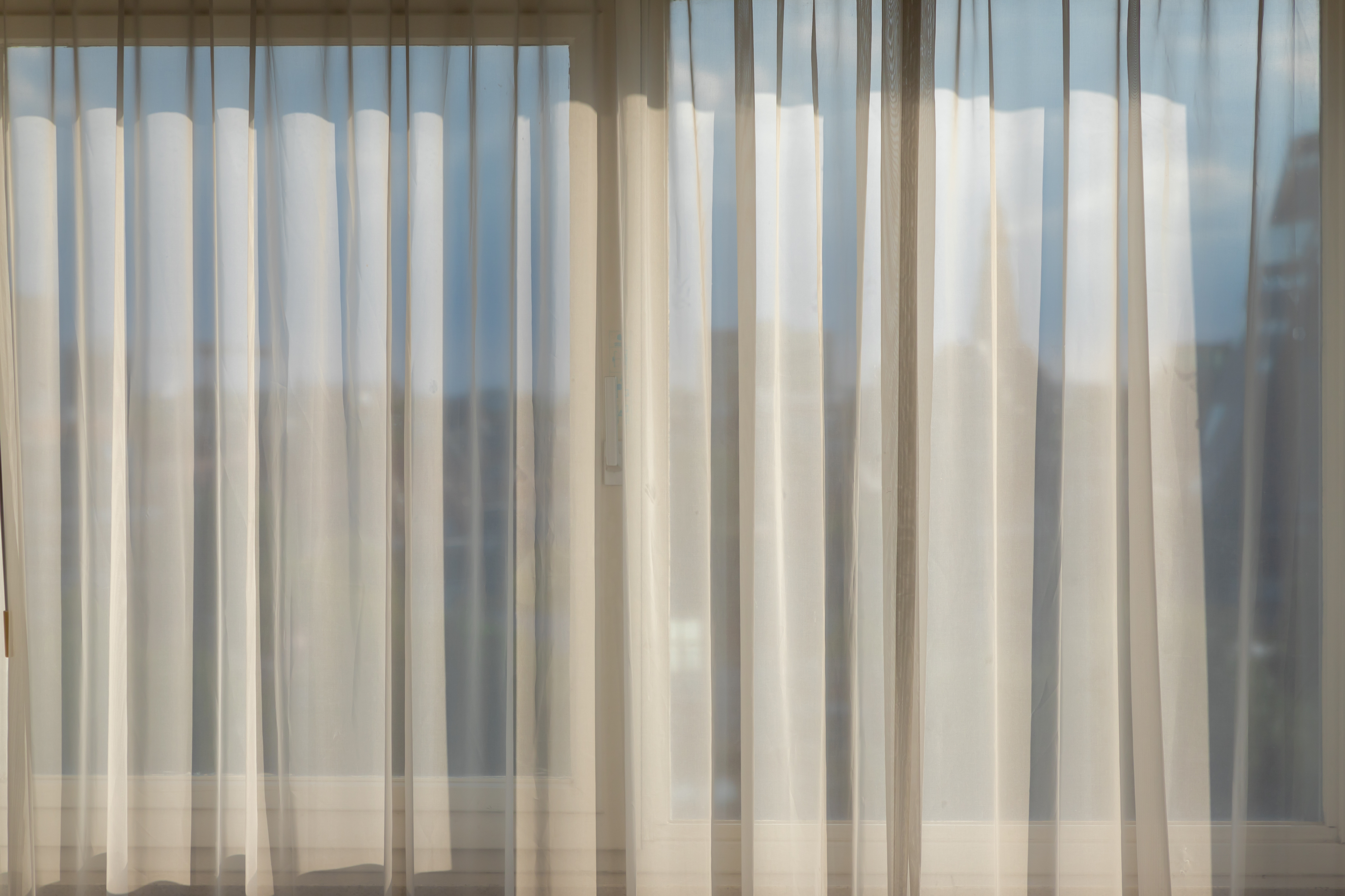Sheer white curtains softening afternoon light in a quiet room, a gentle image for a hard grieving day at home