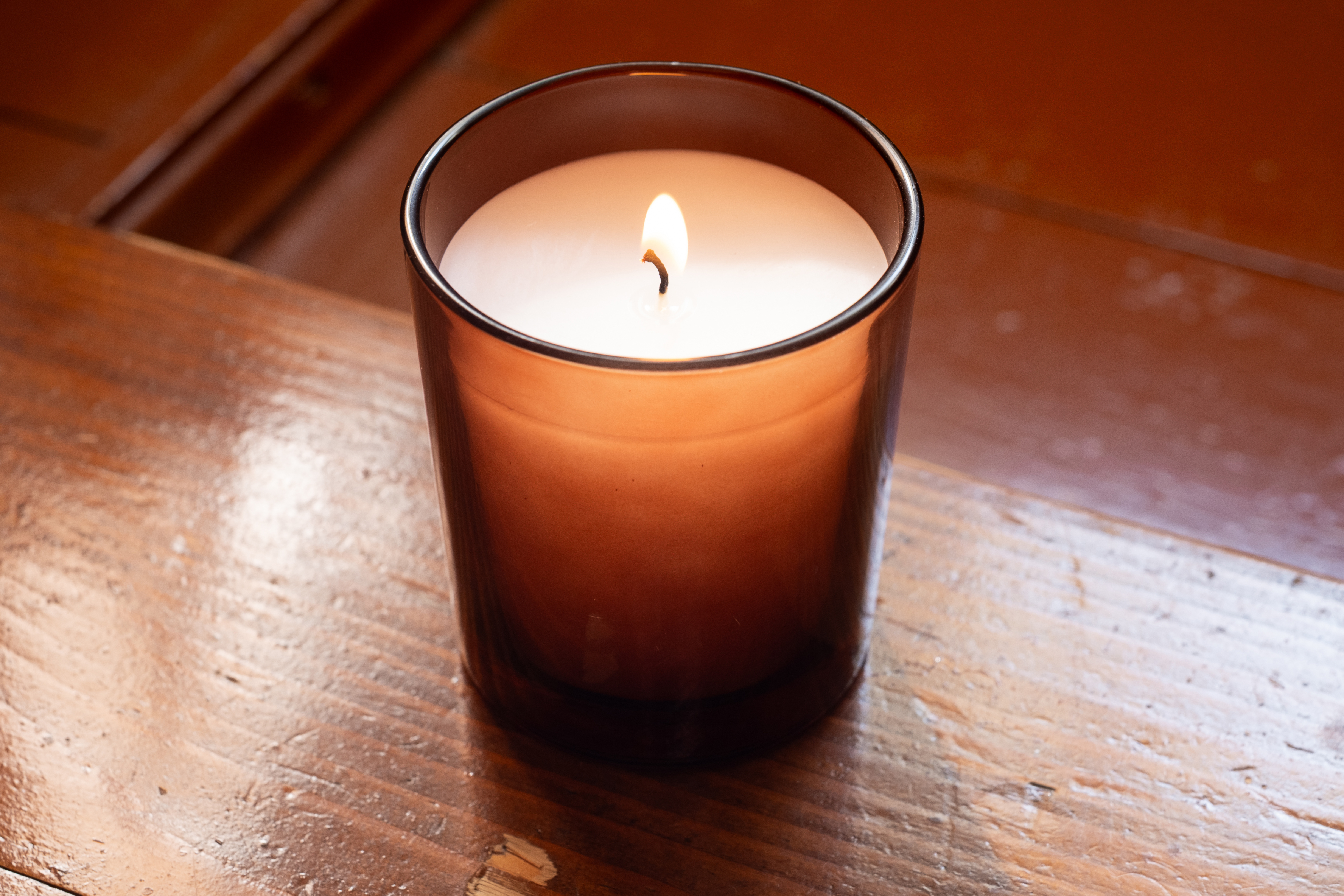 A single lit candle glowing warmly in an amber glass jar in a dim, calm room