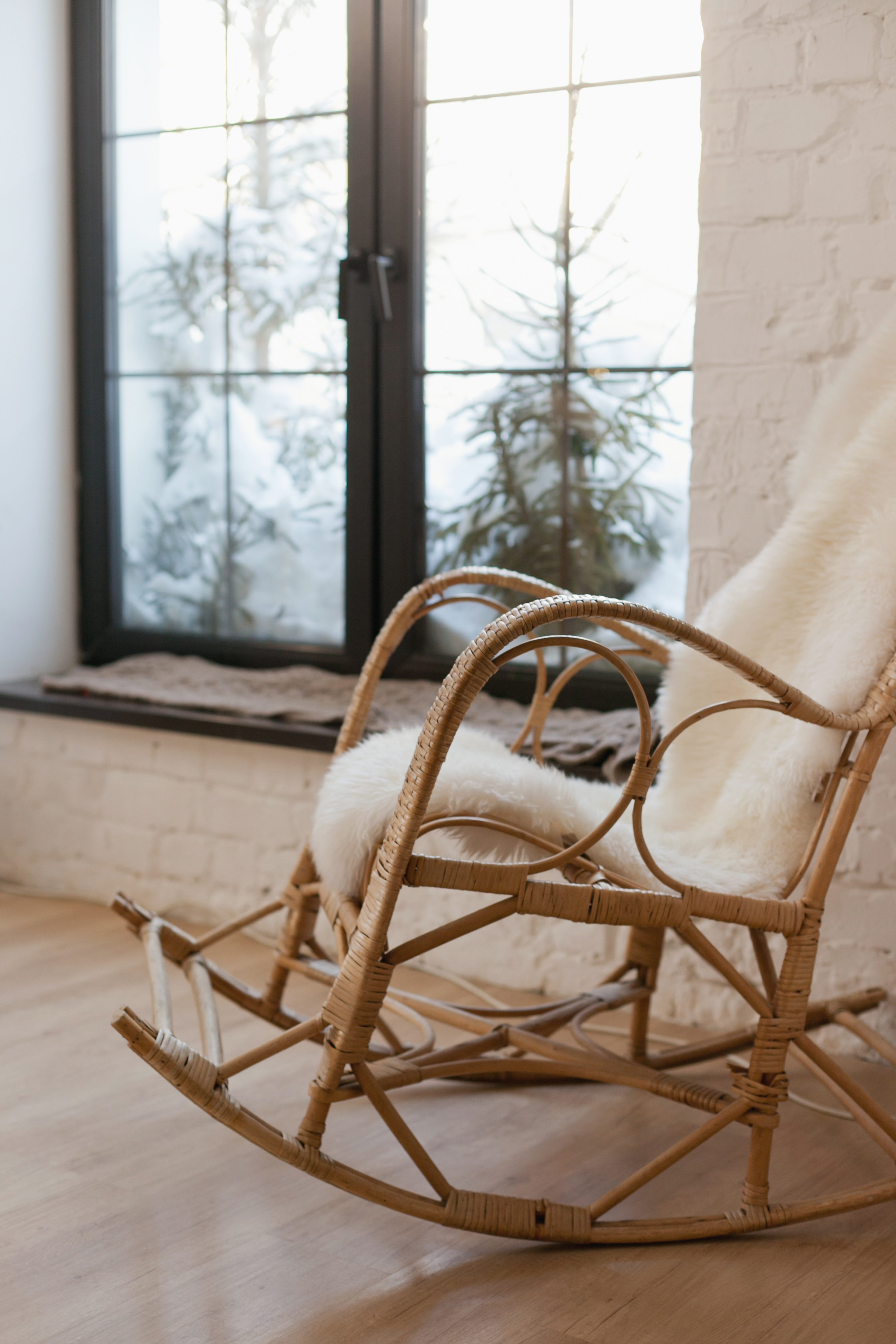 A soft wooden rocking chair resting by tall sunlit windows in a quiet, peaceful room filled with gentle morning light