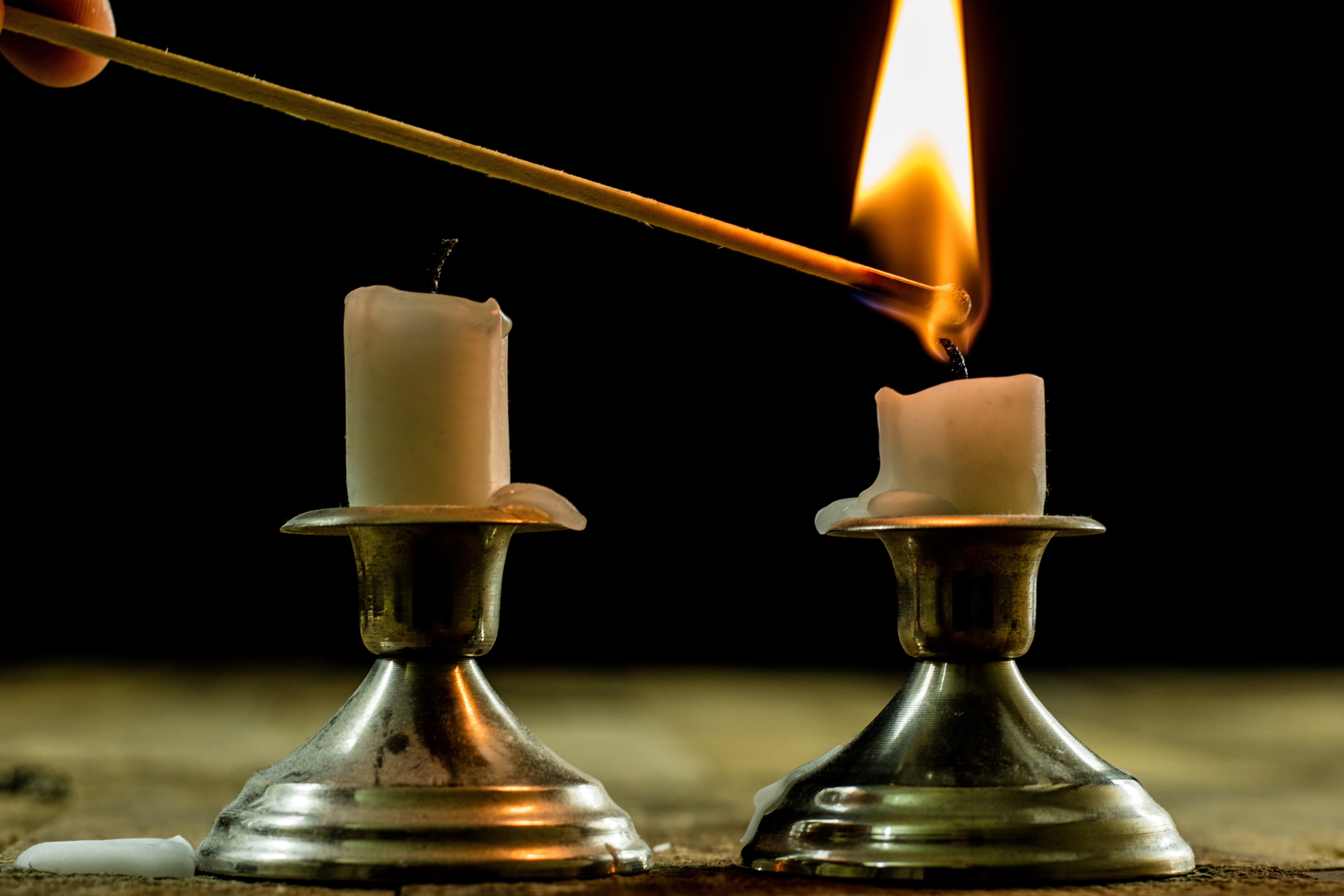 Two candles burning quietly in candlesticks on a worn wooden table, a simple way some families mark a hard moment at home
