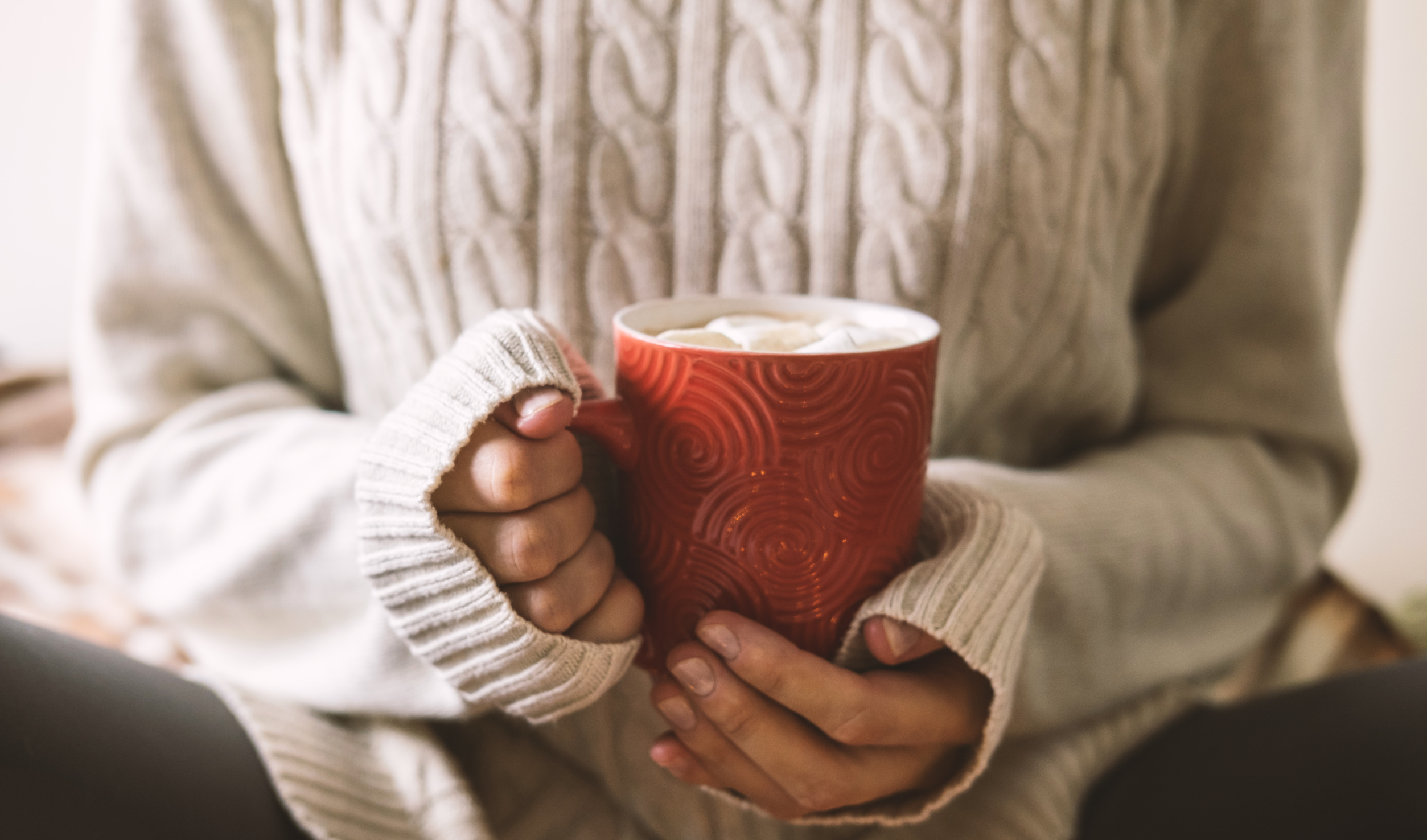 Two hands in a soft knit sweater wrapped around a warm mug, resting still, the kind of small pause that helps on a foggy grieving day