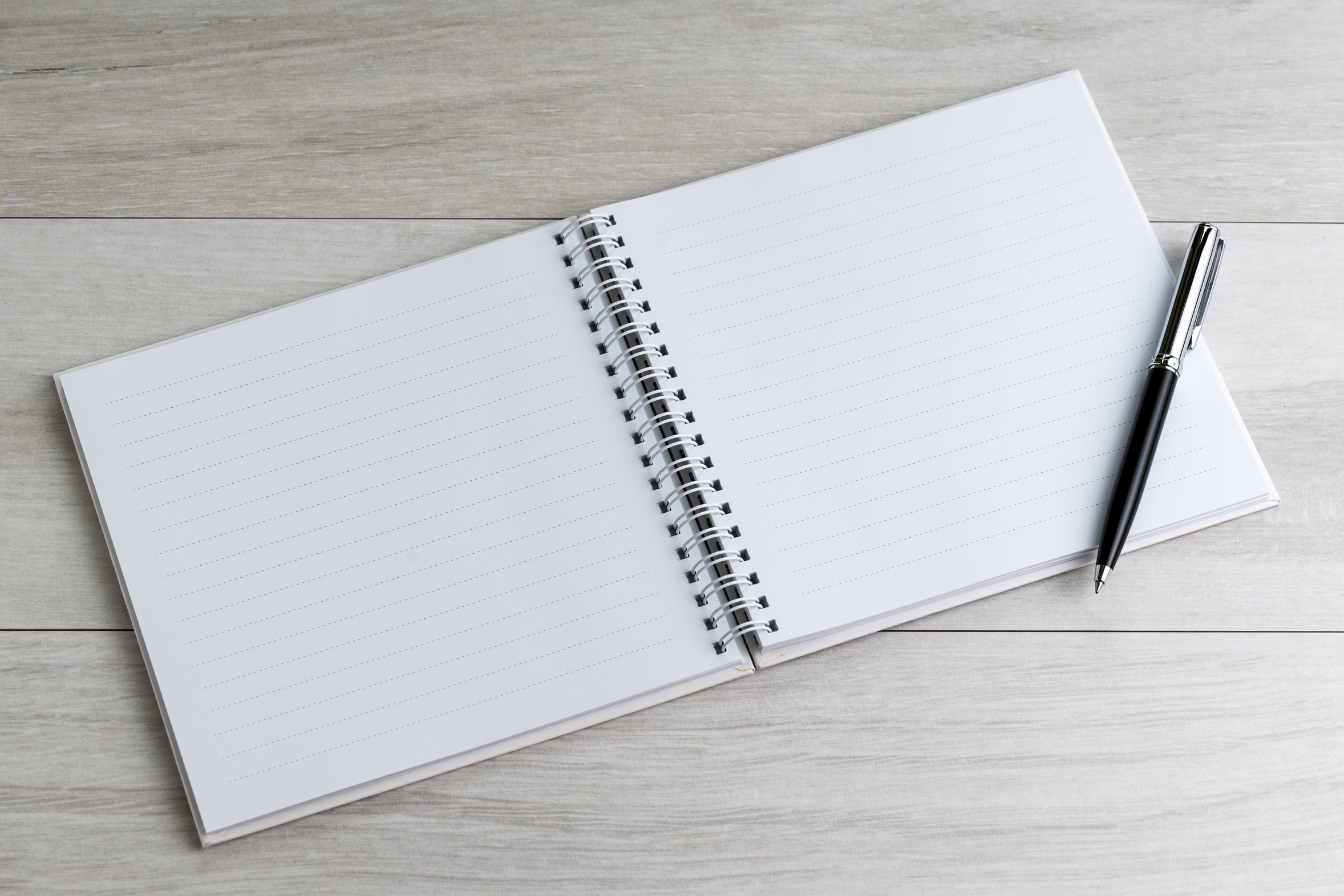 An open notebook and a pen waiting on a pale wooden table, somewhere to write down what a tired mind cannot hold onto right now
