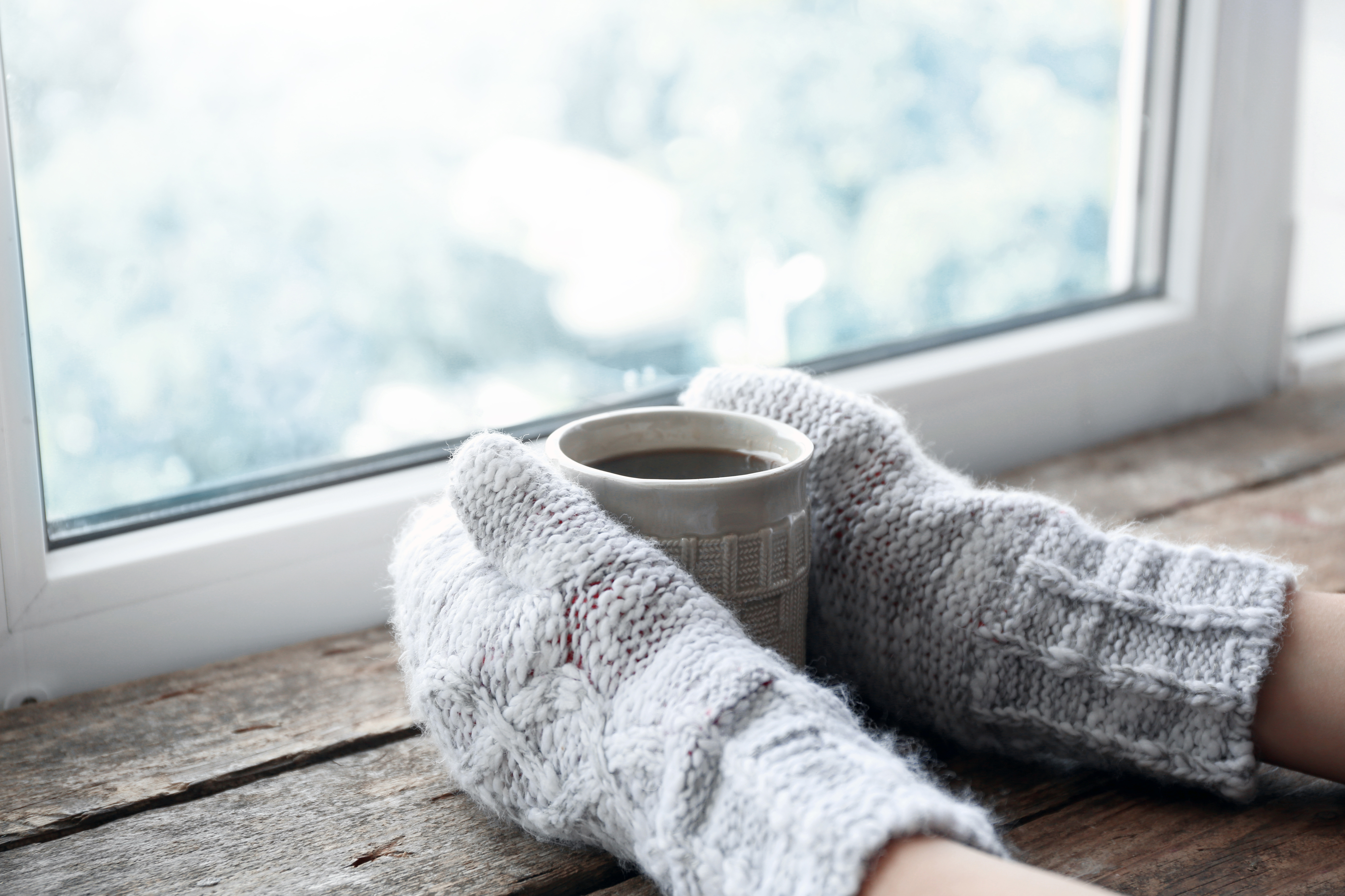 Two hands cradling a warm mug on a bright windowsill, a quiet moment alone at home during the holidays after losing a baby