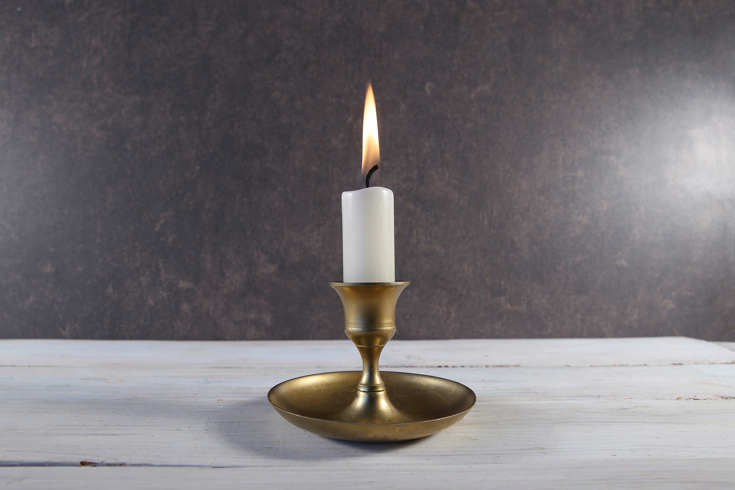A single candle burning in a simple holder on a pale wooden table at home, a quiet way to mark and remember a baby lost early in pregnancy
