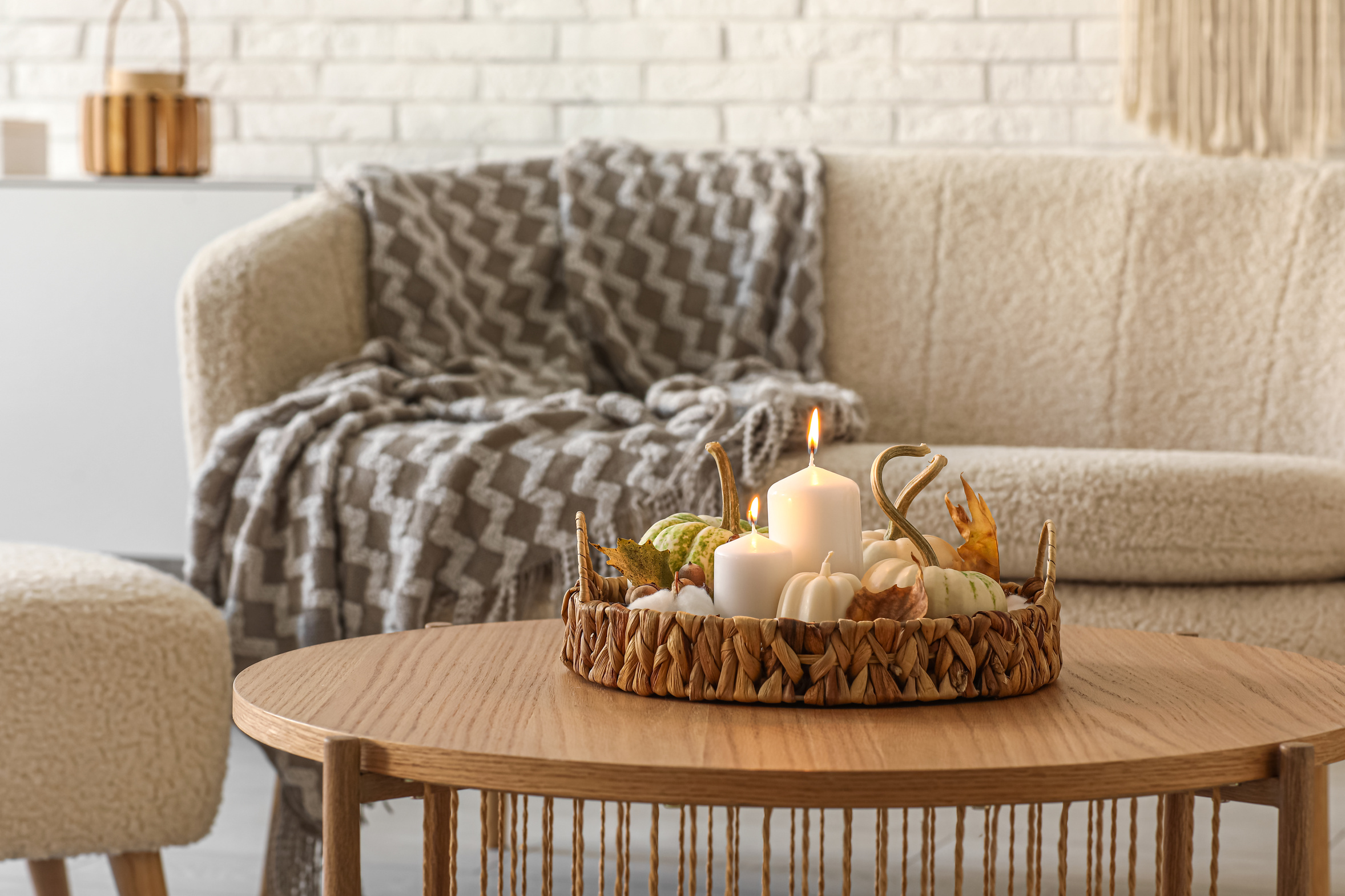 Lit candles, small pumpkins and autumn leaves arranged on a wicker tray on a wooden table in a quiet, softly lit room at home